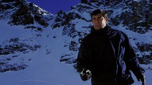 James Bond, warmly dressed, is standing against a backdrop  of snowy mountains. He is pointing a gun at someone off screen.