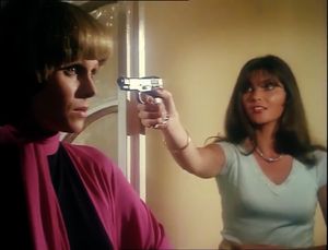 In the foreground, Purdey is in shadow, looking fixedly ahead. In the background, a dark-haired woman is pointing a gun at her.