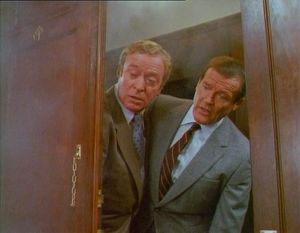 Roger Moore and Michael Caine are in a wood-panelled corridor on the Orient Express. They have opened the door to look into one  of the cabins, which is filled with smoke.