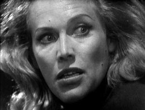 A tight closeup photo in black and white of Honor Blackman's face. Her hair is wild and she looks tense, as if she's just seen something.