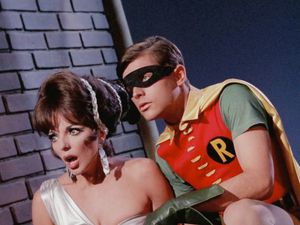 In a photo taken with the usual Dutch angle, Robin is crouching next to Lorelei Circe, played by Joan Collins in a silver dress. Her mouth is open, as if she's singing.