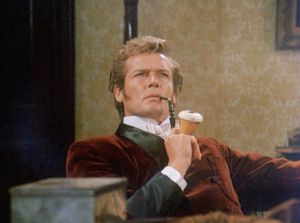 Roger Moore is dressed as Sherlock Holmes, sitting in an armchair in the sitting room, smoking a pipe.